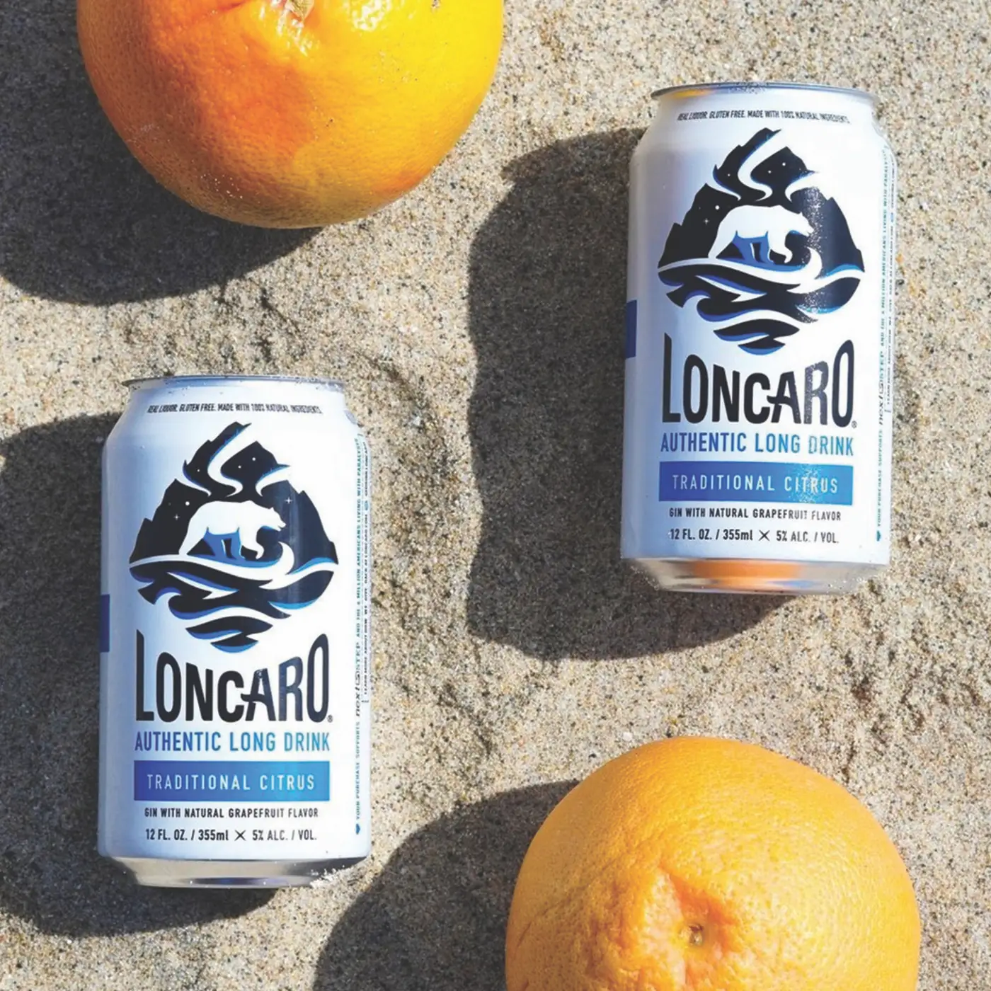 Two cans of citrus Loncaro in the sand with whole grapefruits