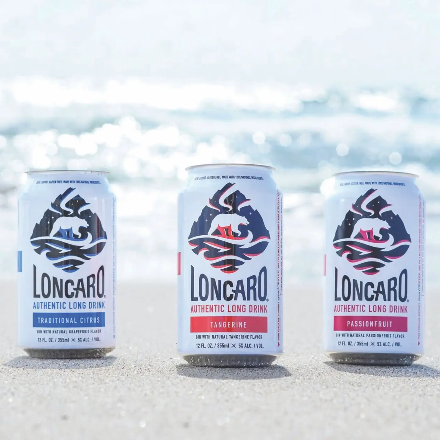 Cans of original, tangerine, and passionfruit Loncaro on a sandy beach